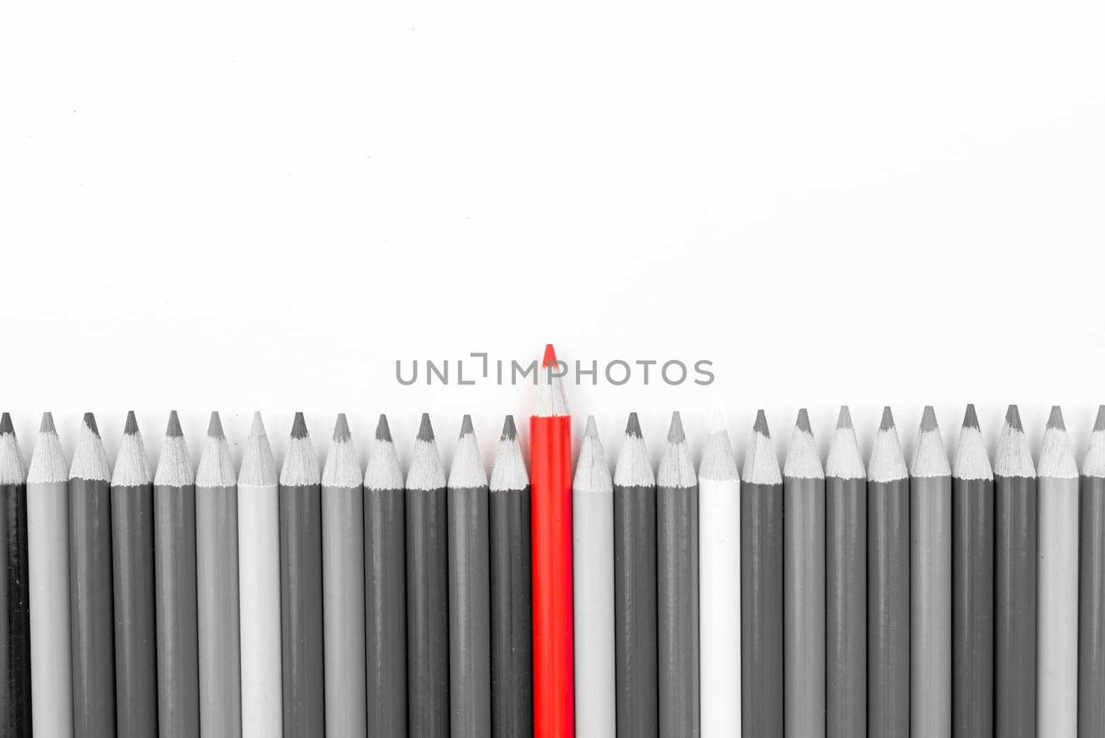 Red pencil standing out from monochrome pencils crowd, copy space available. Stand out from the crowd concept