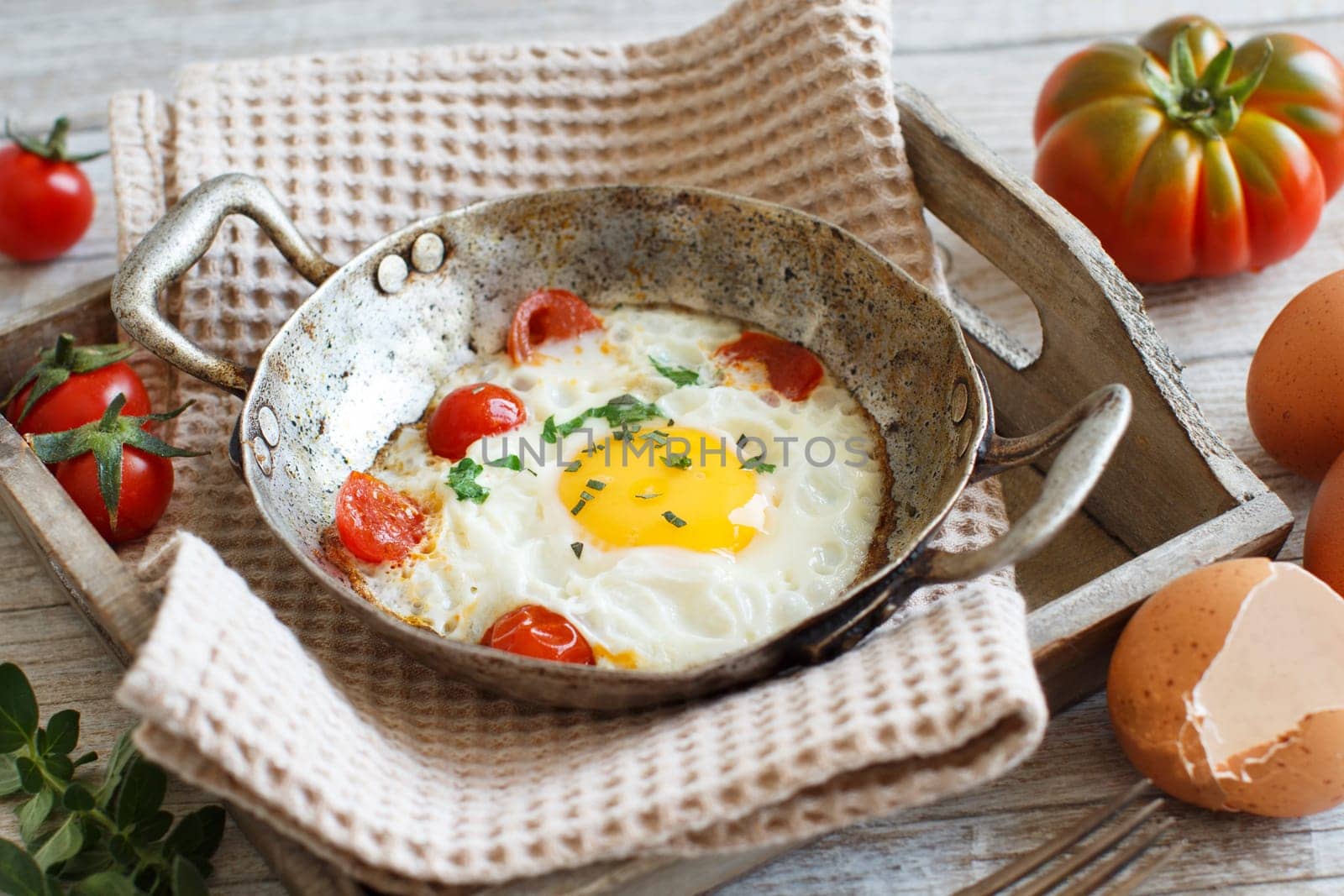 Fried egg with tomatoes and herbs n a old frying pan on wood
