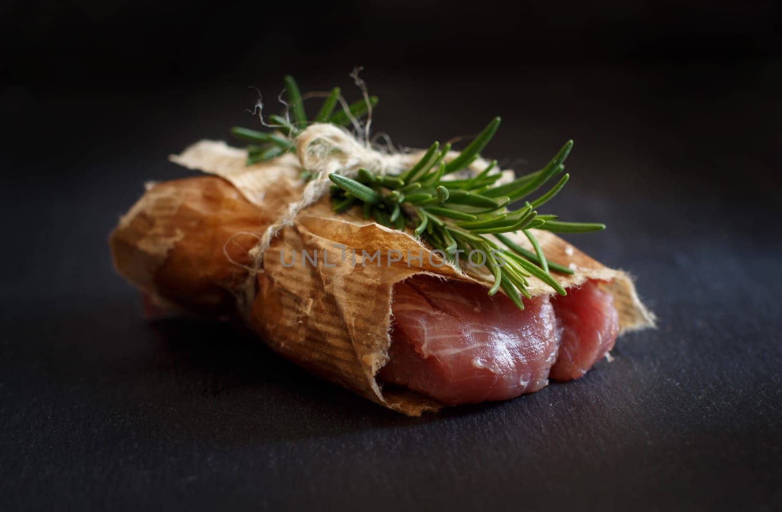 Slice of raw turkey steak with rosemary on dark background