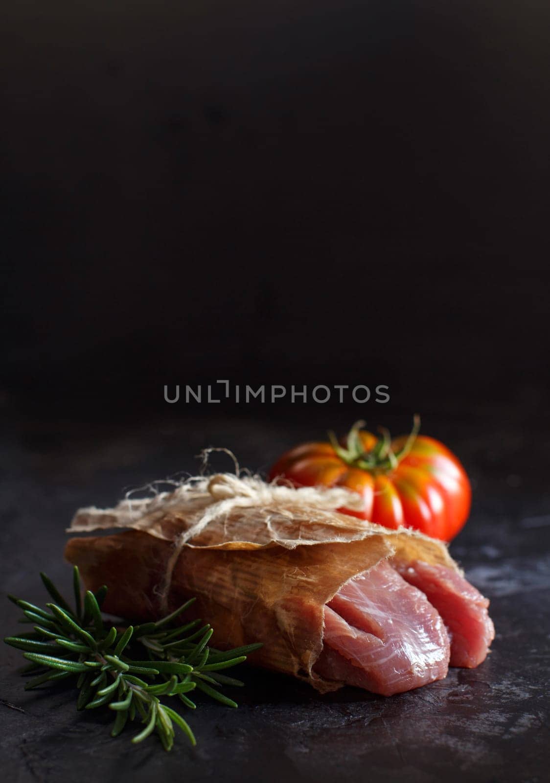 Slice of raw turkey steak with rosemary and tomatoes on dark background