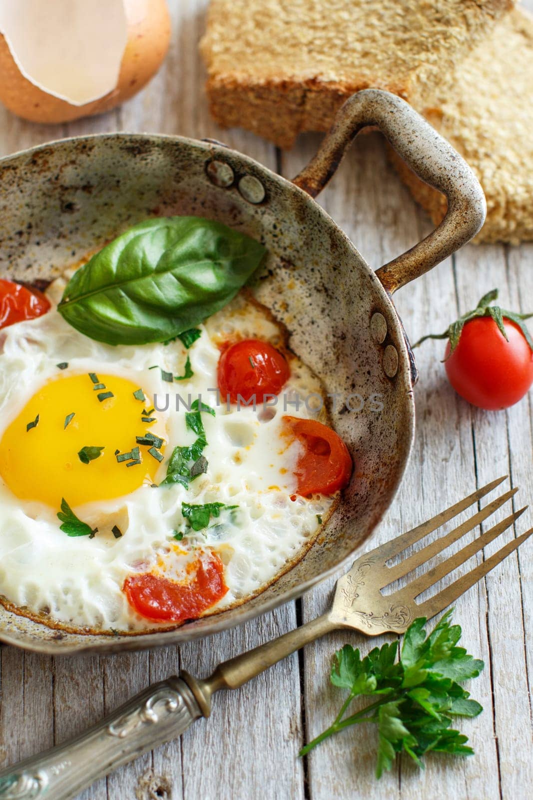 Fried egg with tomatoes, homemade bread and herbs on a old frying pan on wood