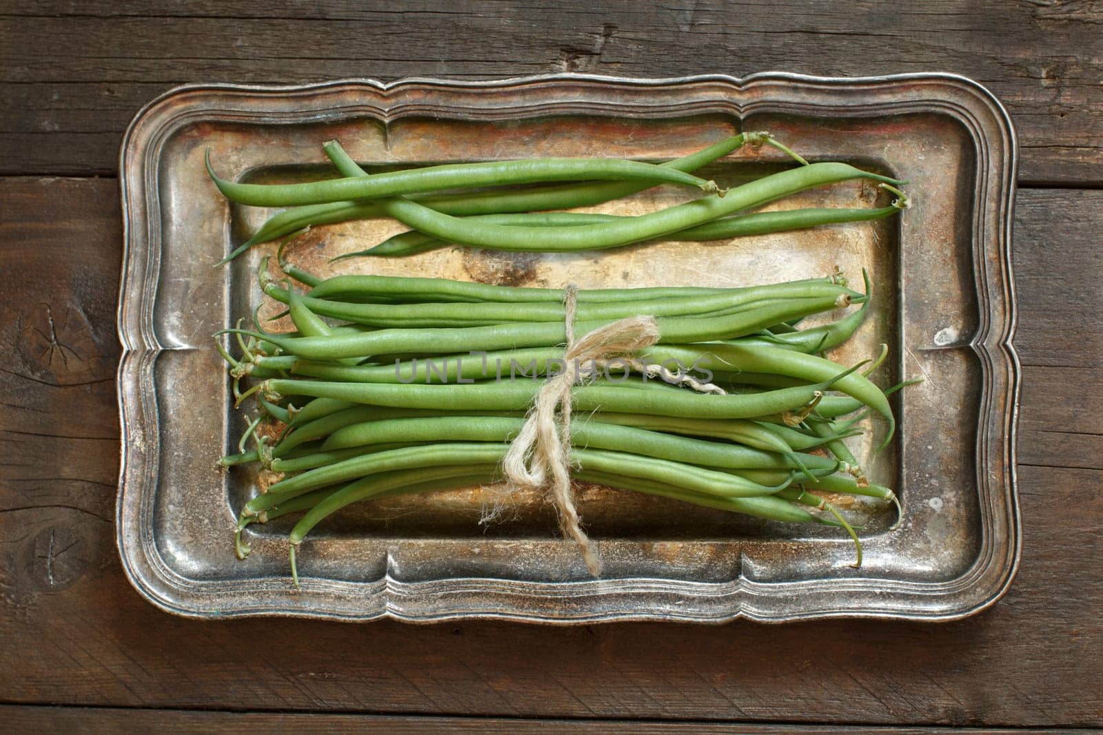 Fresh green french beans on a metal tray on wooden background