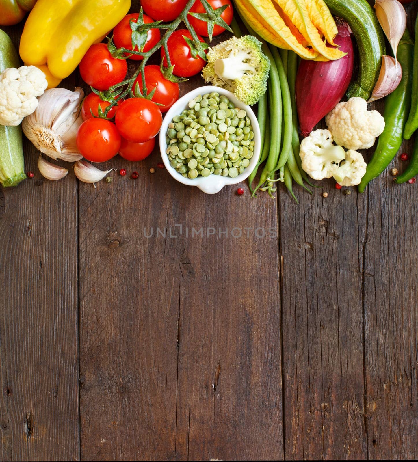 Green peas in a bowl with fresh vegetables on wood top view