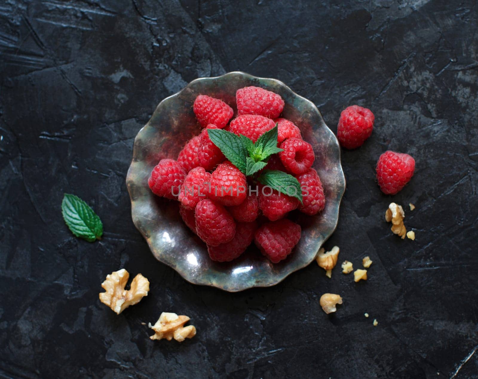 Raspberries, walnuts and mint leaves on dark background top view
