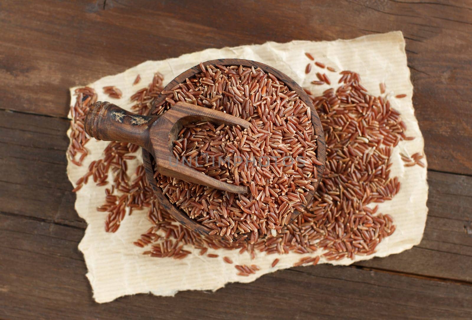 Uncooked Red rice in a bowl with a wooden spoon on the table