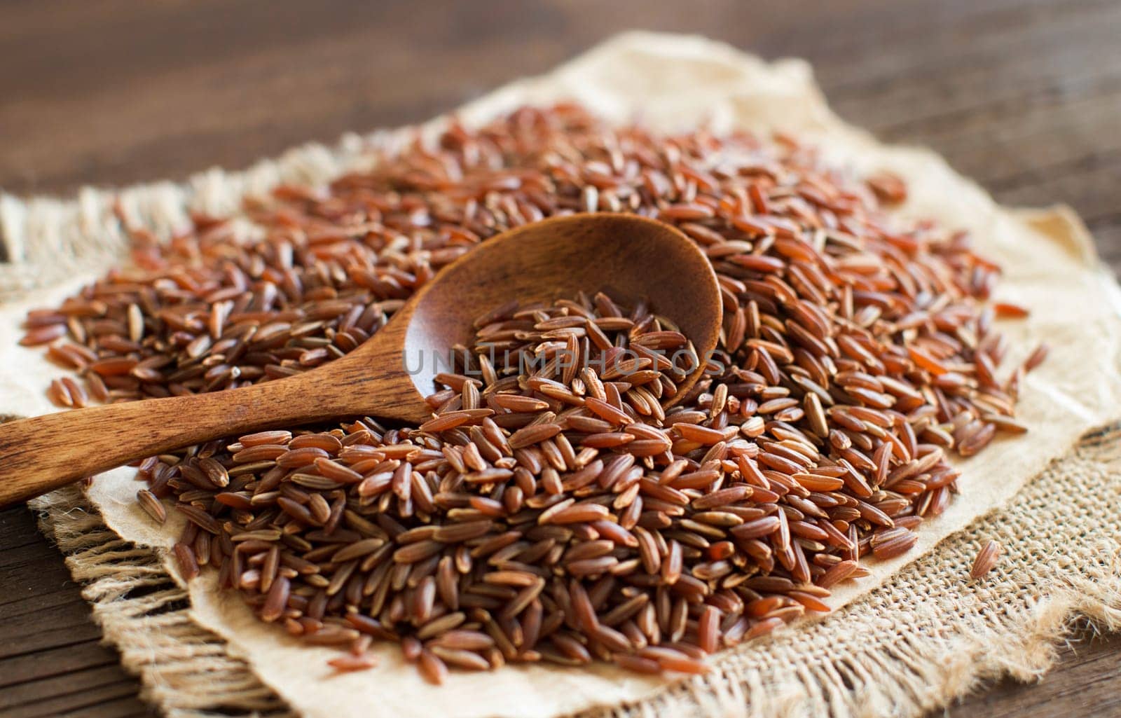Uncooked Red rice with a wooden spoon close up
