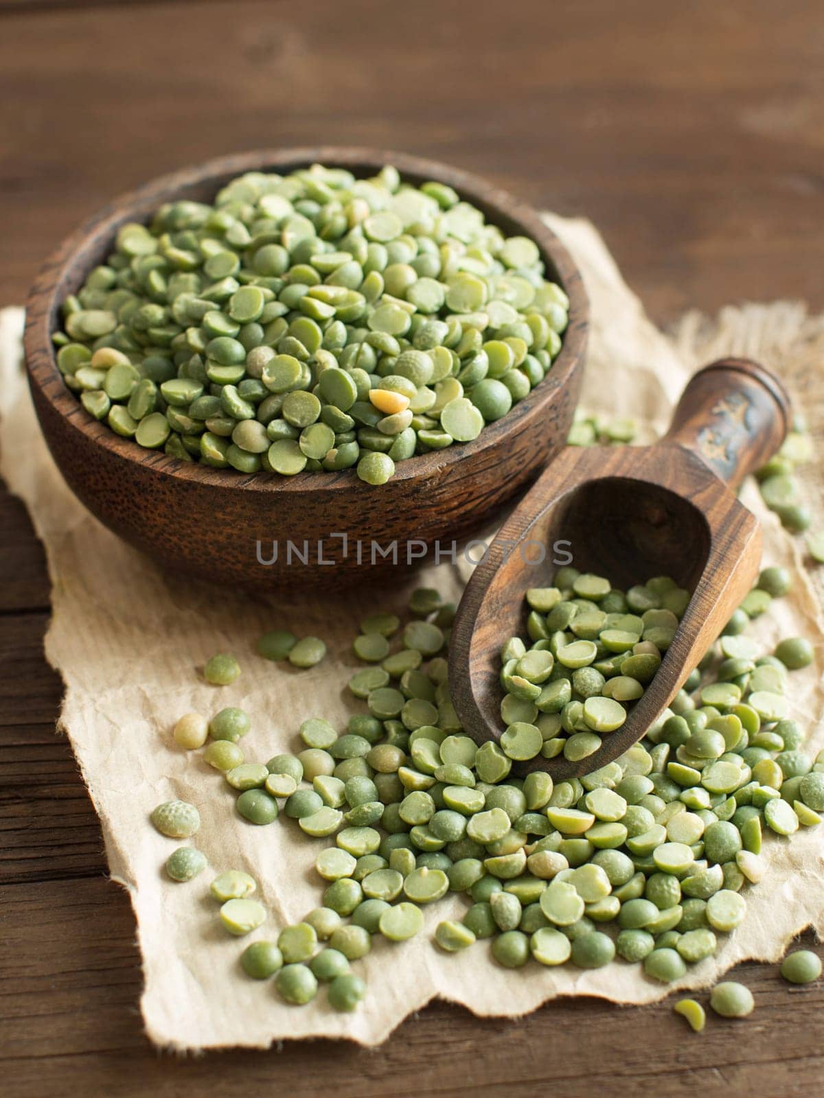 Uncooked Green Split Peas in a bowl with a spoon on a wooden table