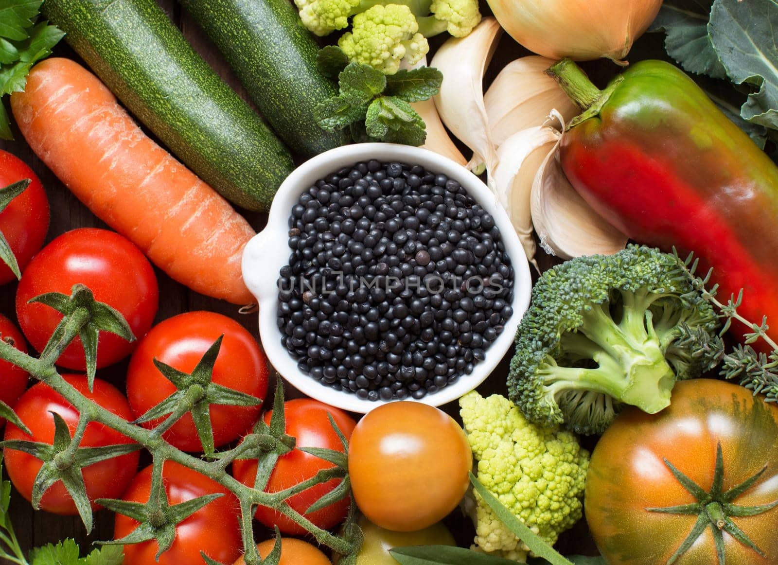 Uncooked black lentils in a bowl with vegetables isolated on white