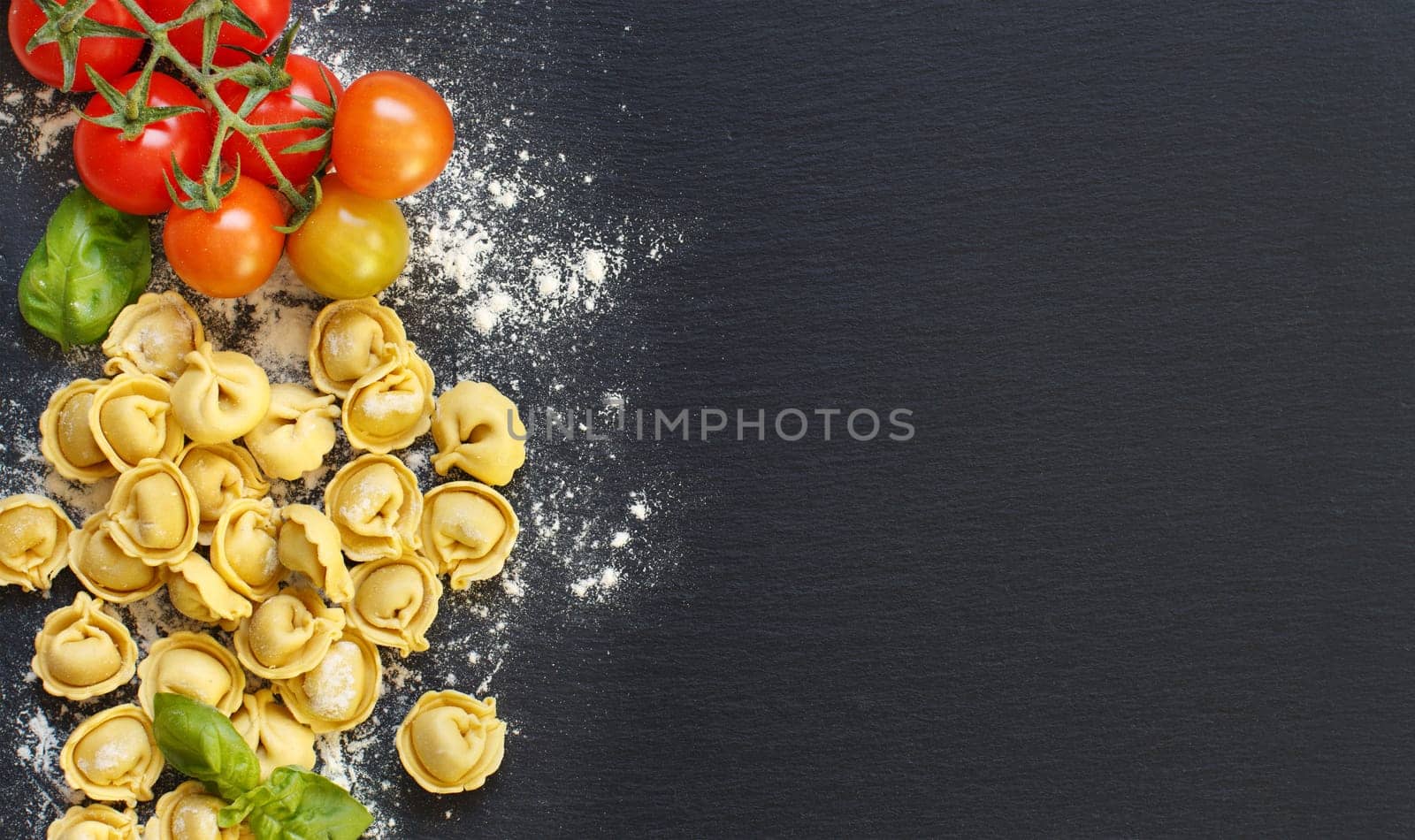 Fresh tortellini with basil ad tomatoes on a dark board top view
