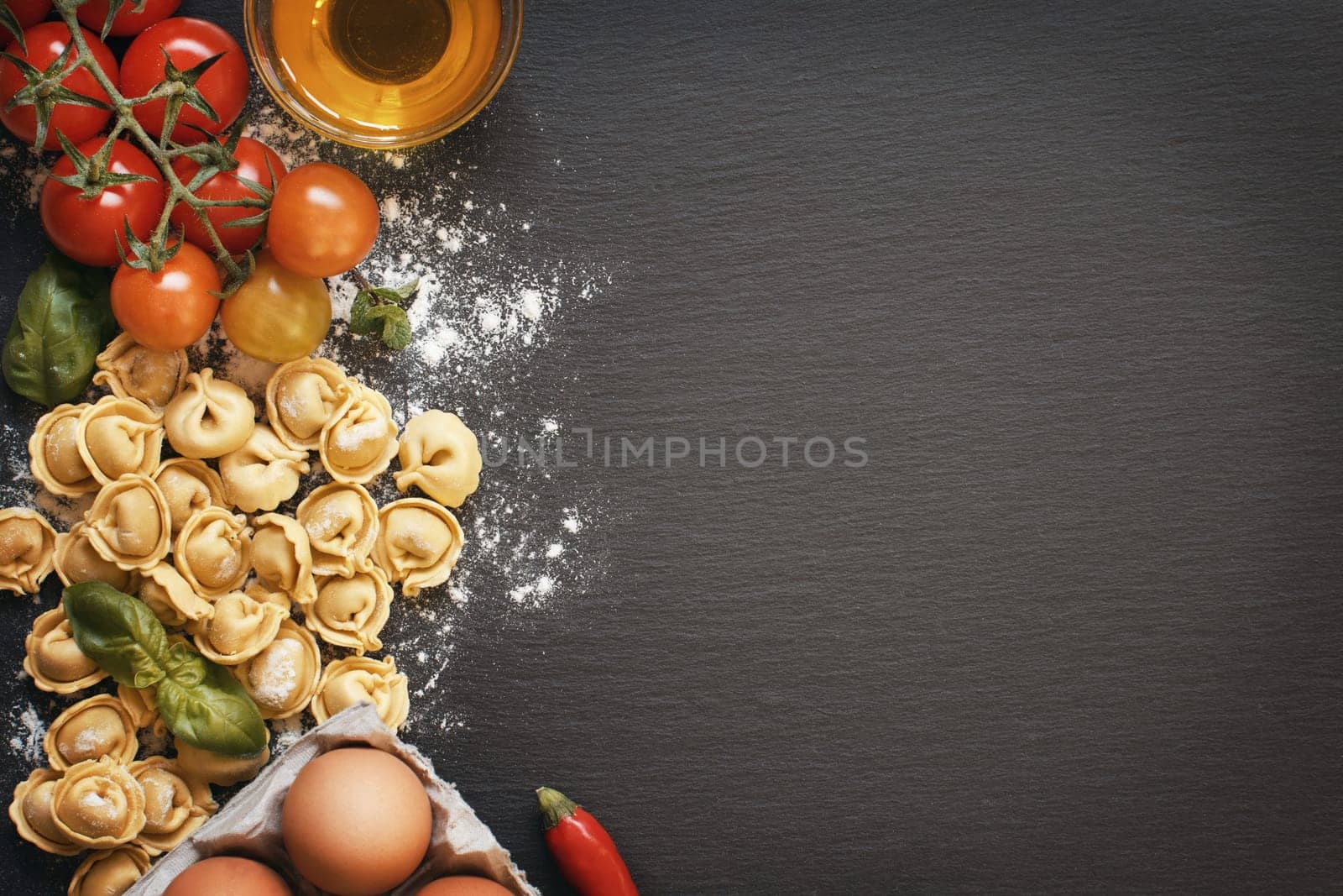 Fresh tortellini pasta and ingredients on a dark board top view