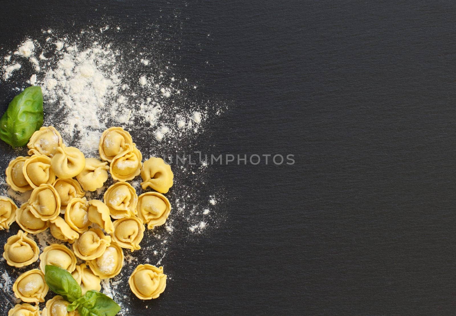 Homemade raw Italian tortellini and basil on a dark background
