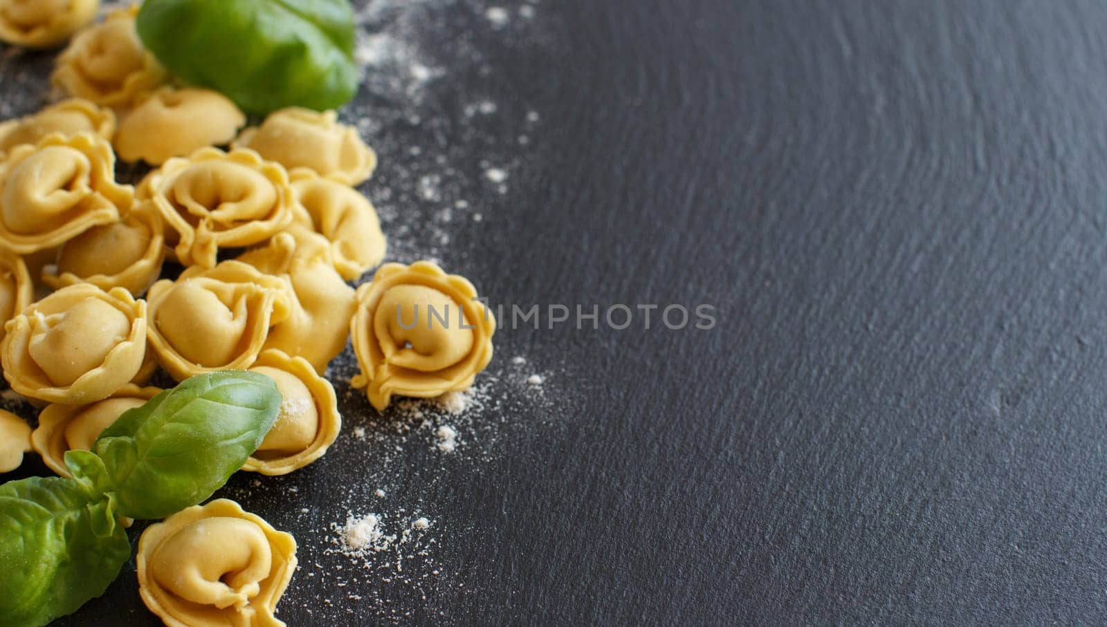 Homemade raw Italian tortellini and basil on a dark background