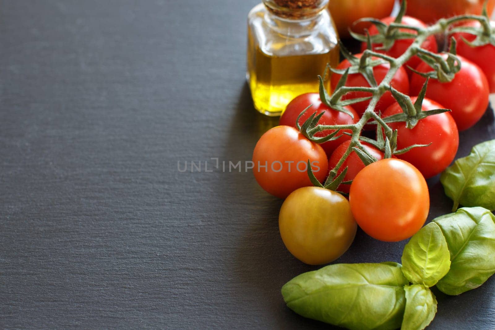 Cherry tomatoes, basil and olive oil on a dark background