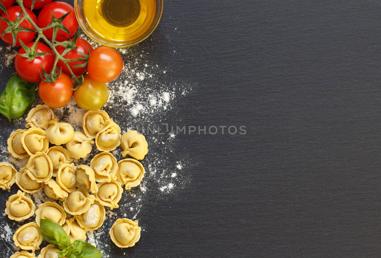 Fresh tortellini pasta and ingredients on a dark board top view