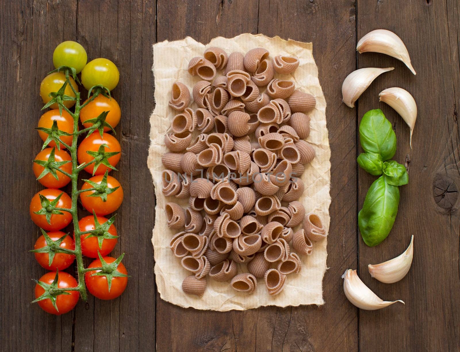 Raw conchiglie pasta, basil and vegetables on wooden background