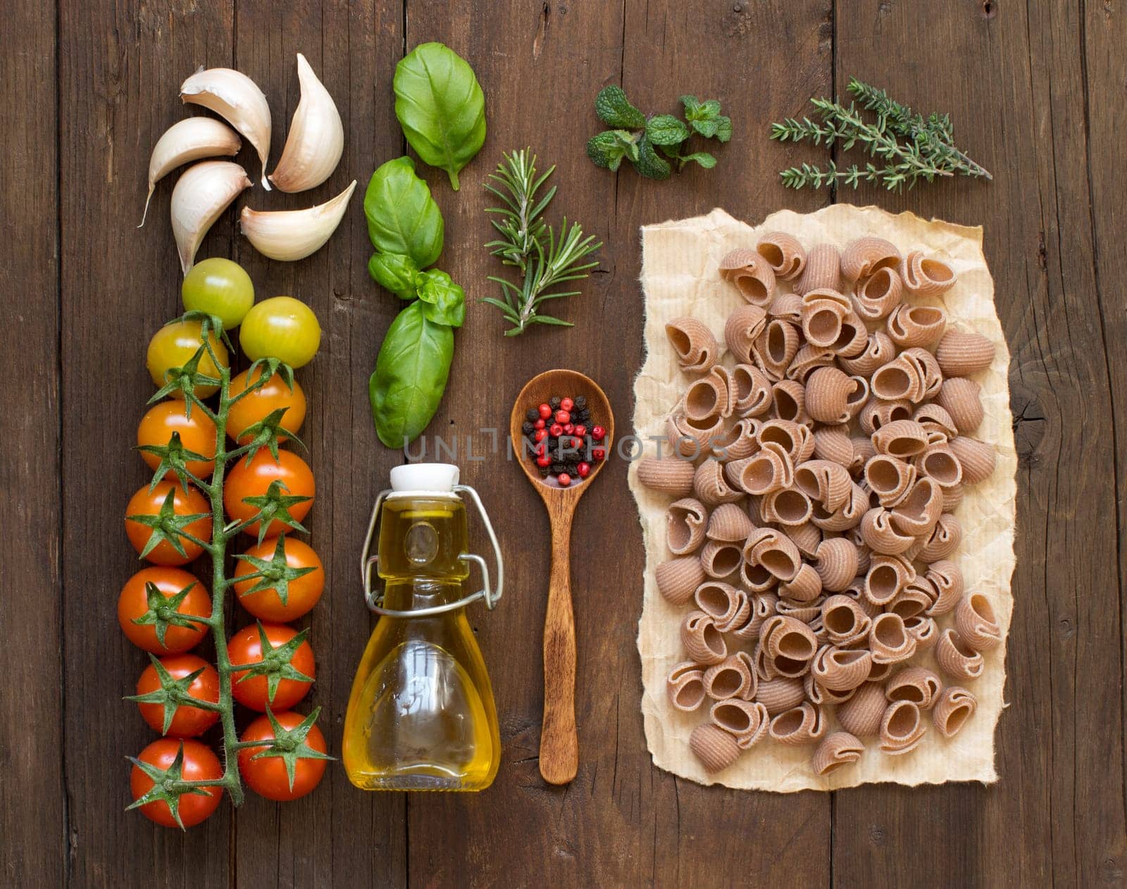 Whole spelt pasta, vegetables, herbs and olive oil on wooden background