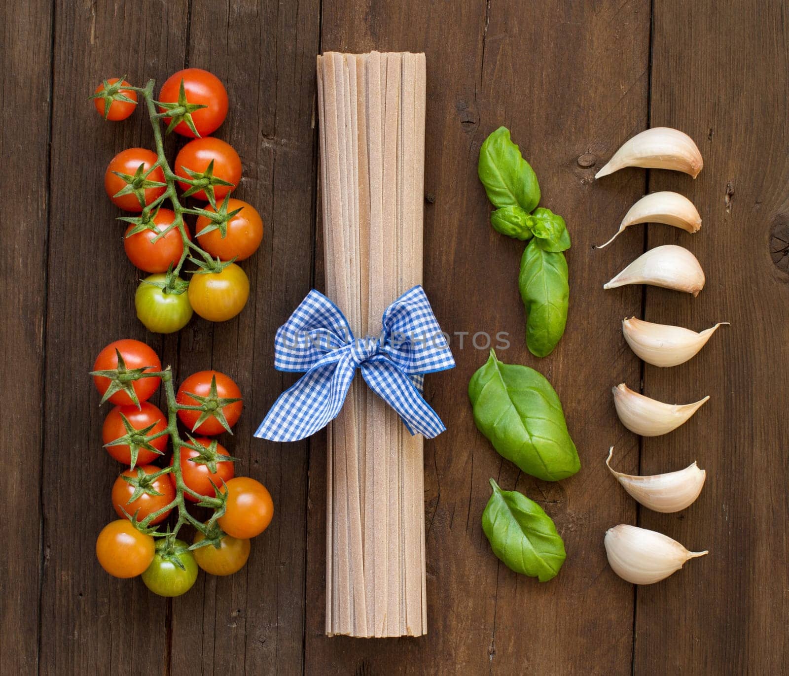 Raw fettucce pasta, basil and vegetables on wooden background