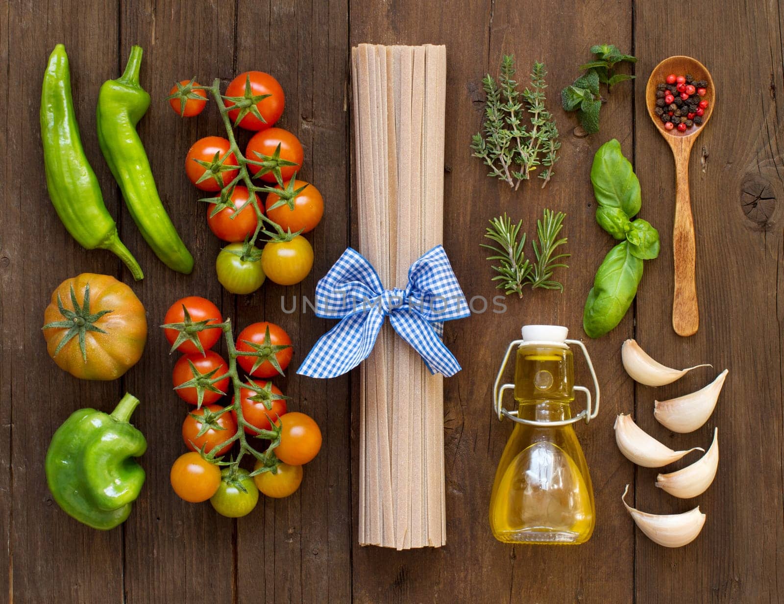 Raw fettucce pasta, vegetables, herbs and olive oil on wooden background