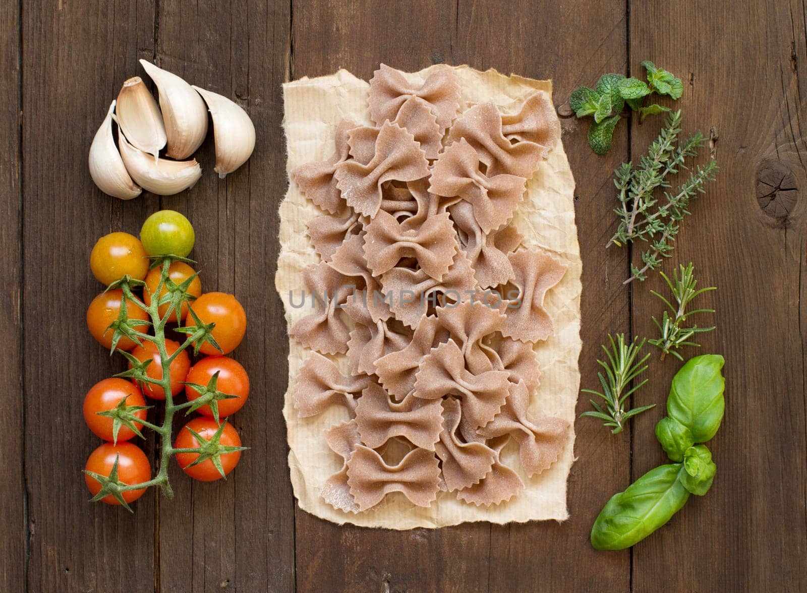 Whole wheat pasta, vegetables and herbs on wooden background