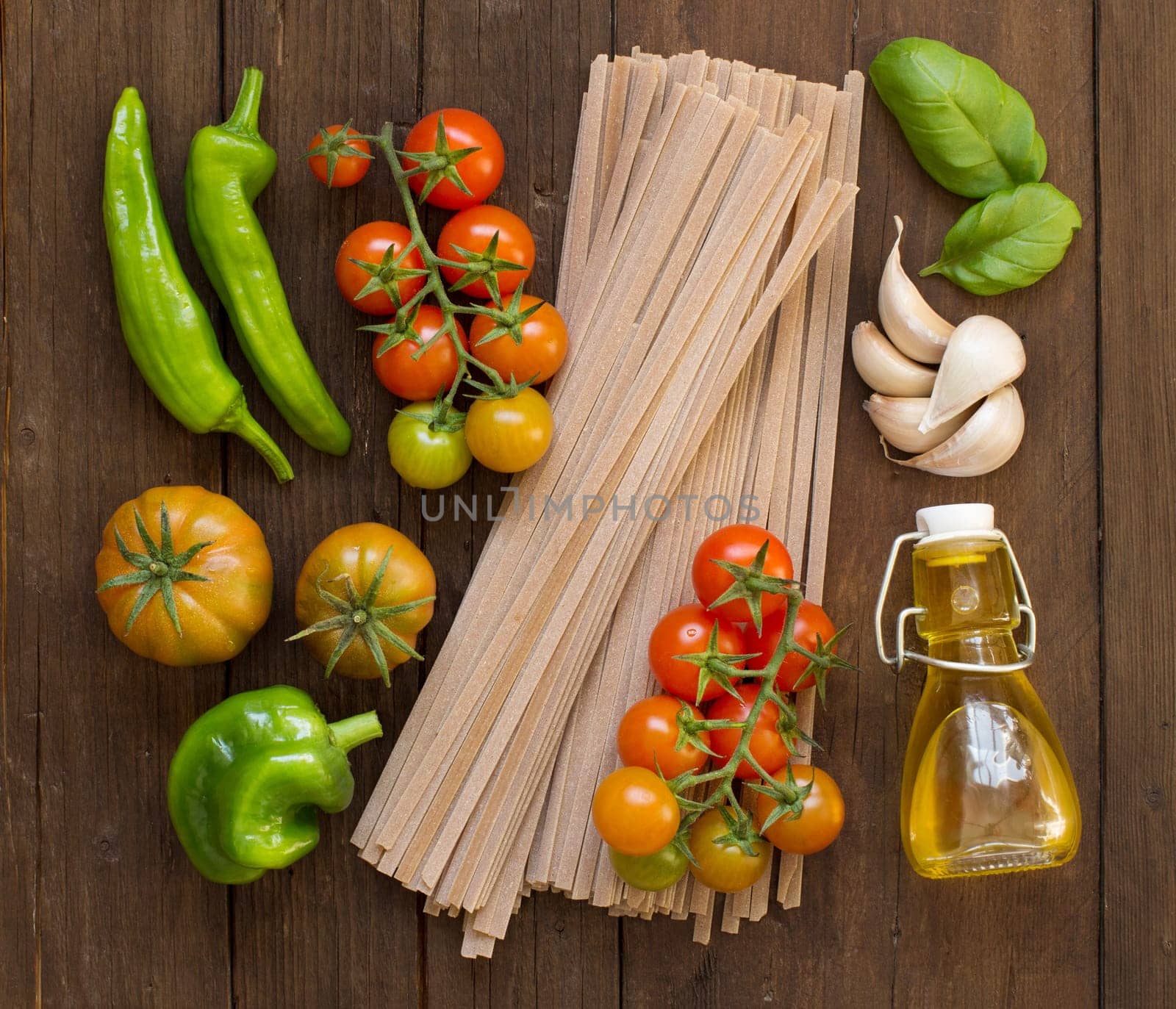 Raw fettucce pasta, vegetables and olive oil on wooden background