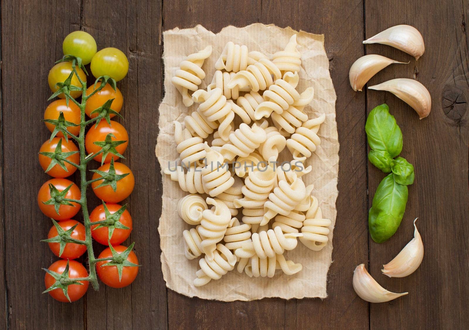 Raw italian pasta, basil and vegetables on wooden background