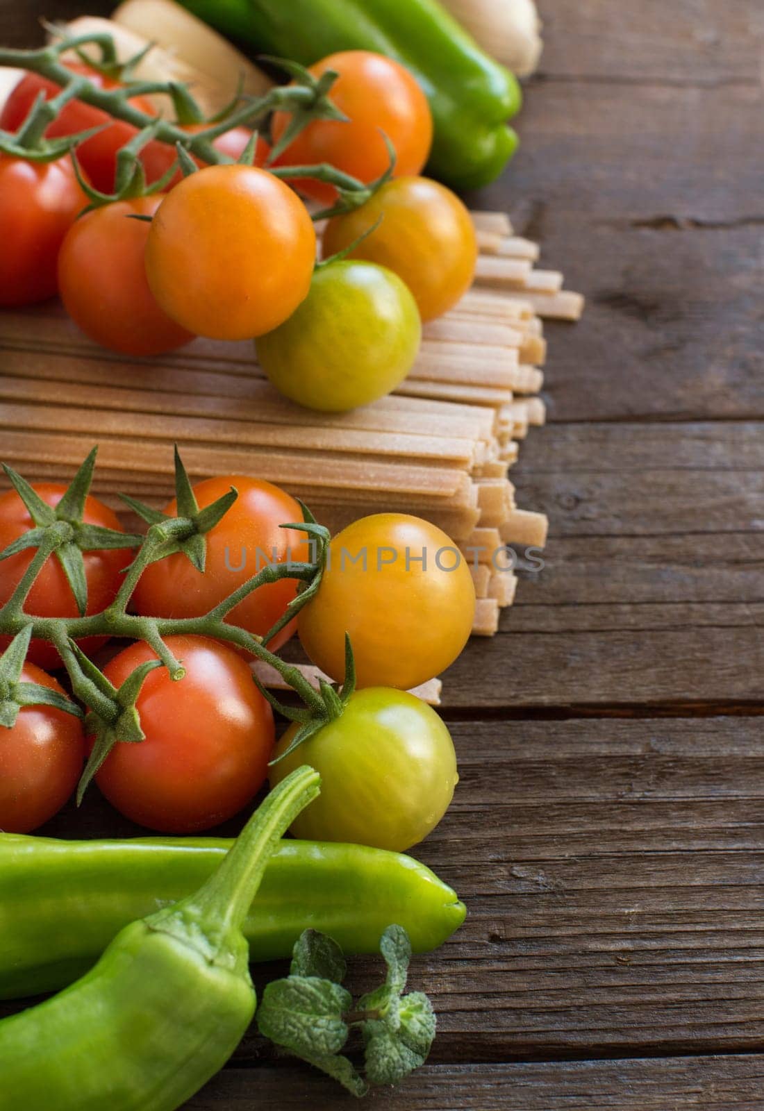 Raw fettucce pasta, vegetables and herbs on wooden background