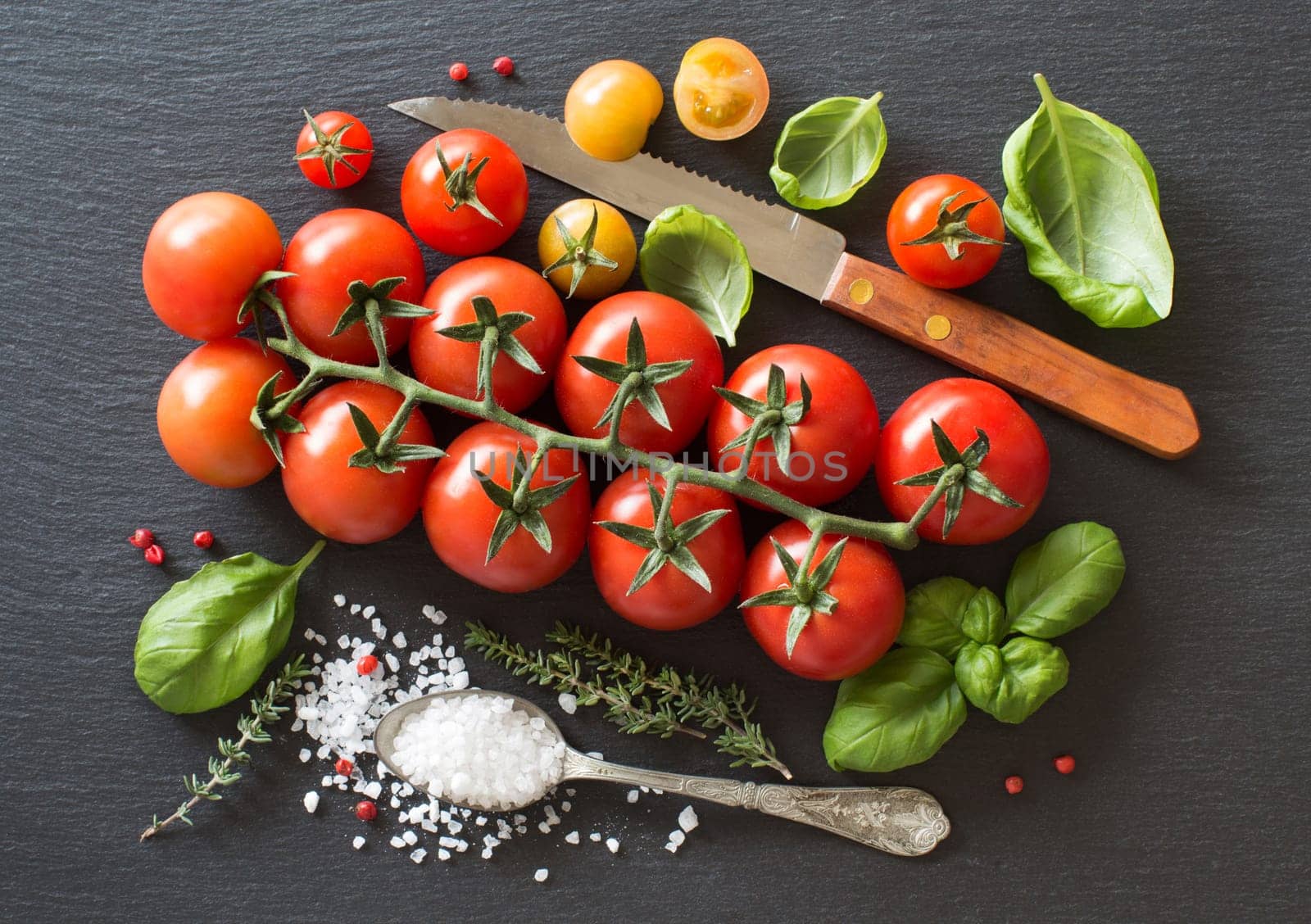 Cherry tomatoes, herbs and salt on a dark board
