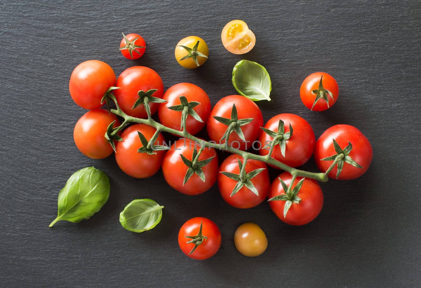 Fresh cherry tomatoes and basil top view on a dark background