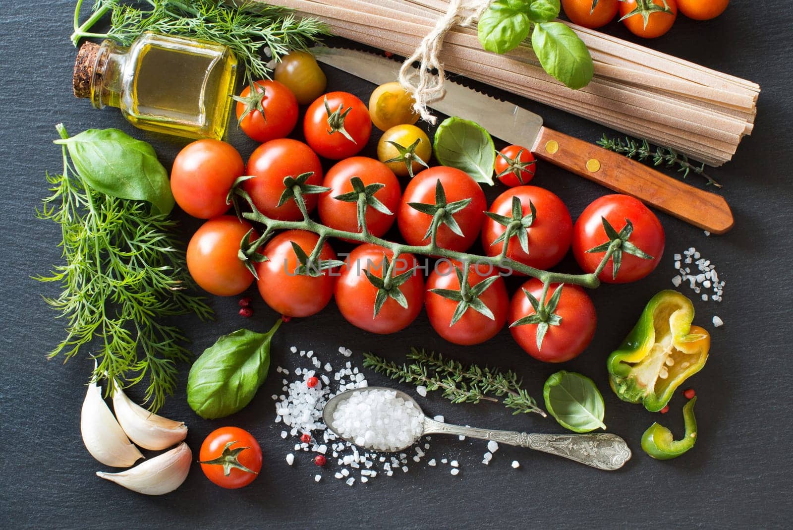 Italian cooking ingridients : cherry tomatoes, herbs, pasta and olive oil on a dark background