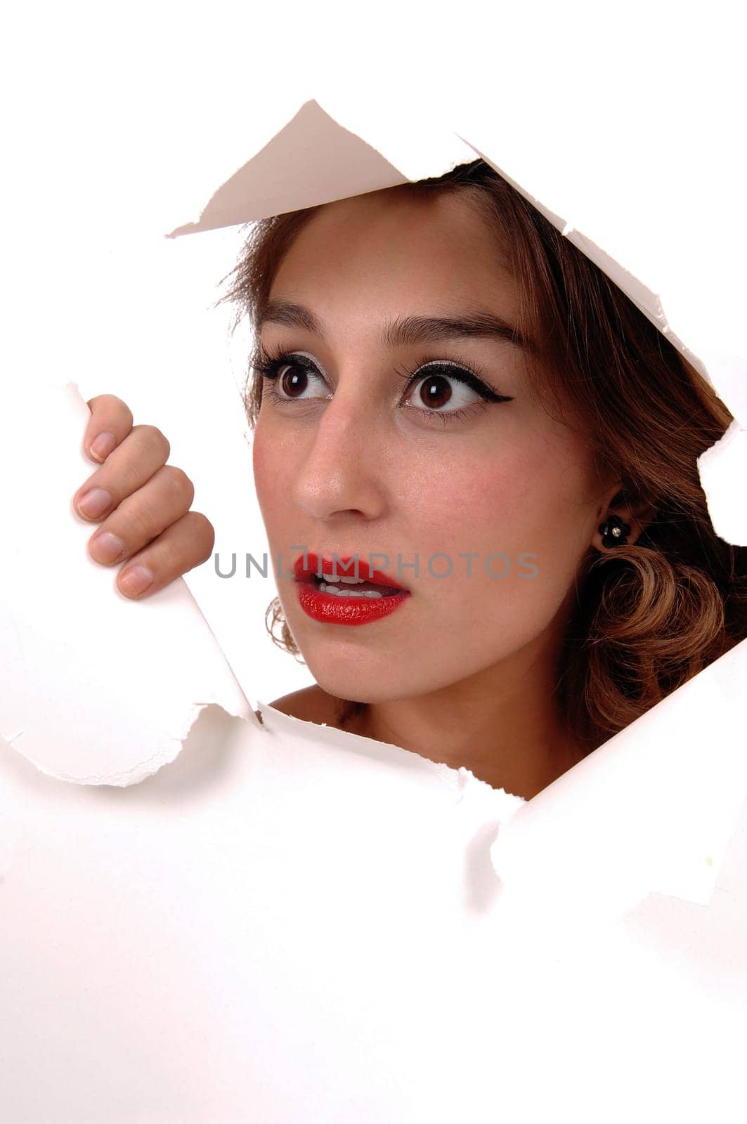 The face of a beautiful young woman showing trough a hole in the .paper, with big eyes, isolated for white background..