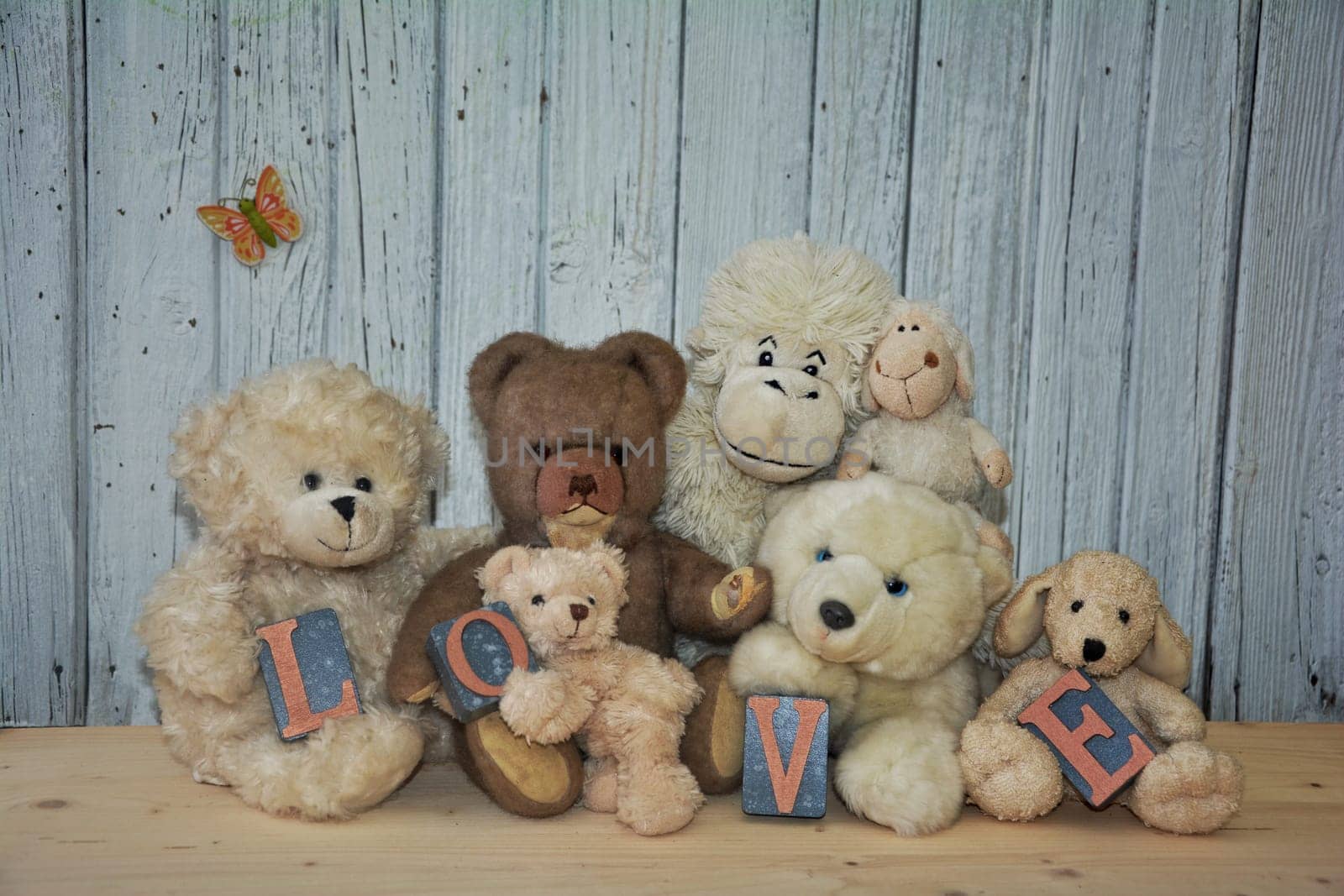 Many teddy bears and stuffed animals with the word Love sit in front of a white wooden wall