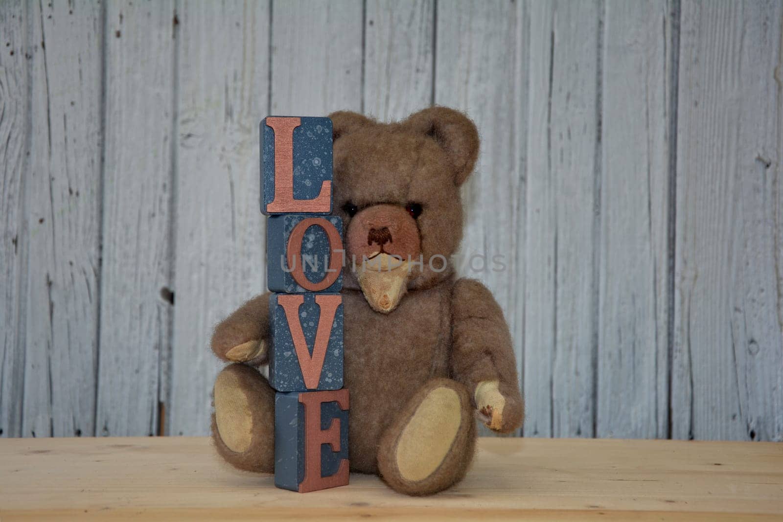 Old antique teddy bear with stacked letter cubes,with the word love in front of old white wooden wall