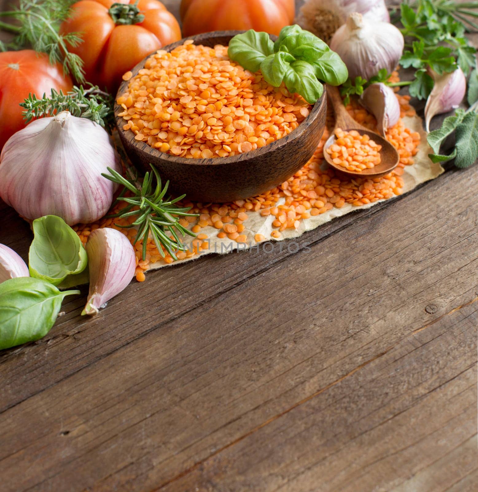 Red lentils in a bowl with tomatoes, garlic and herbs on wood
