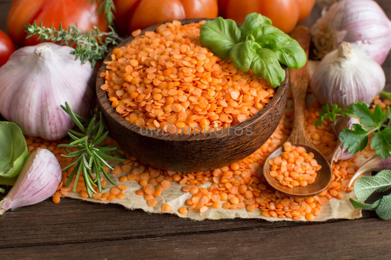 Red lentils in a bowl with tomatoes, garlic and herbs on wood