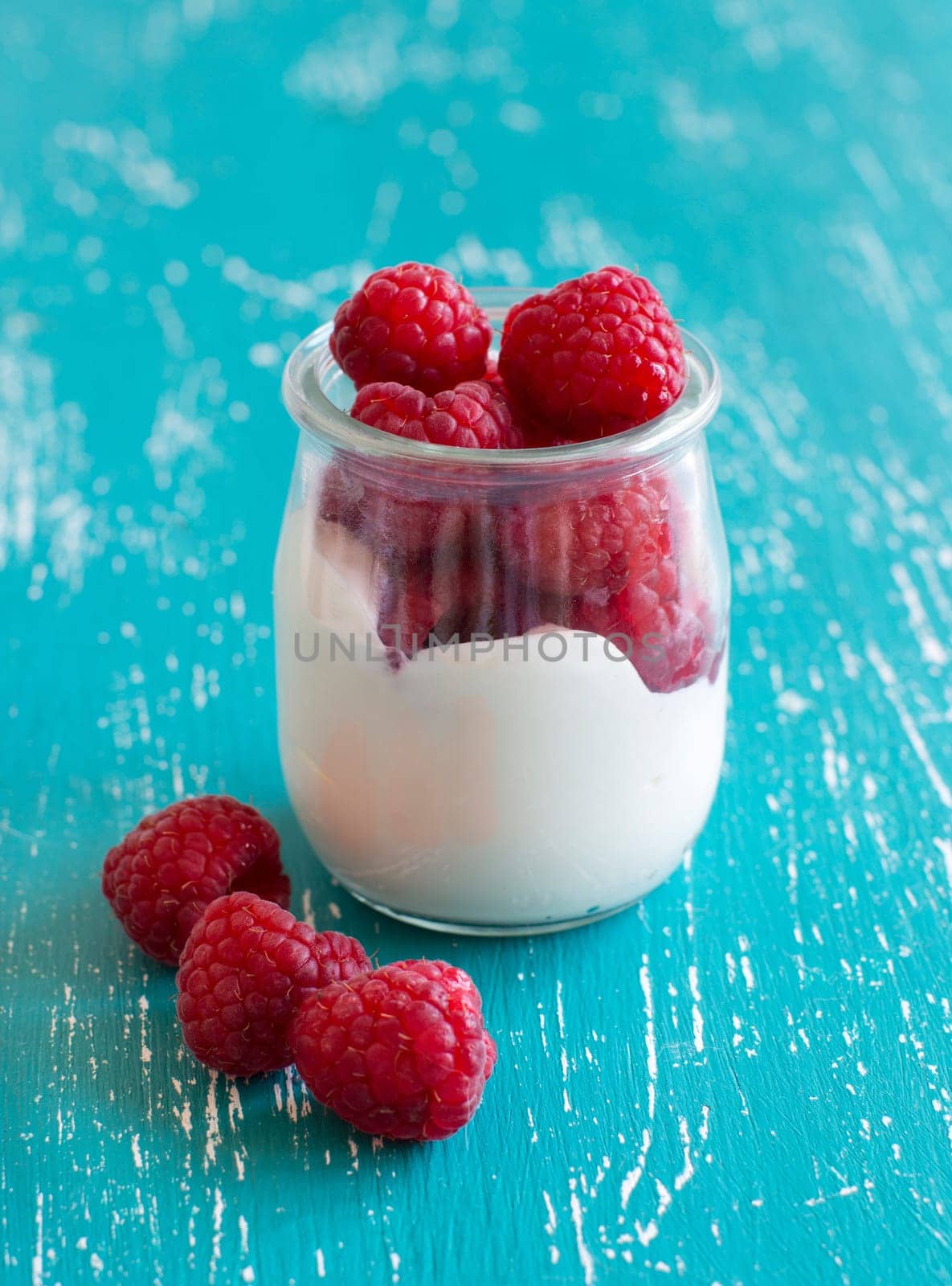 Raspberries and fresh yogurt in a jar on a turquoise background