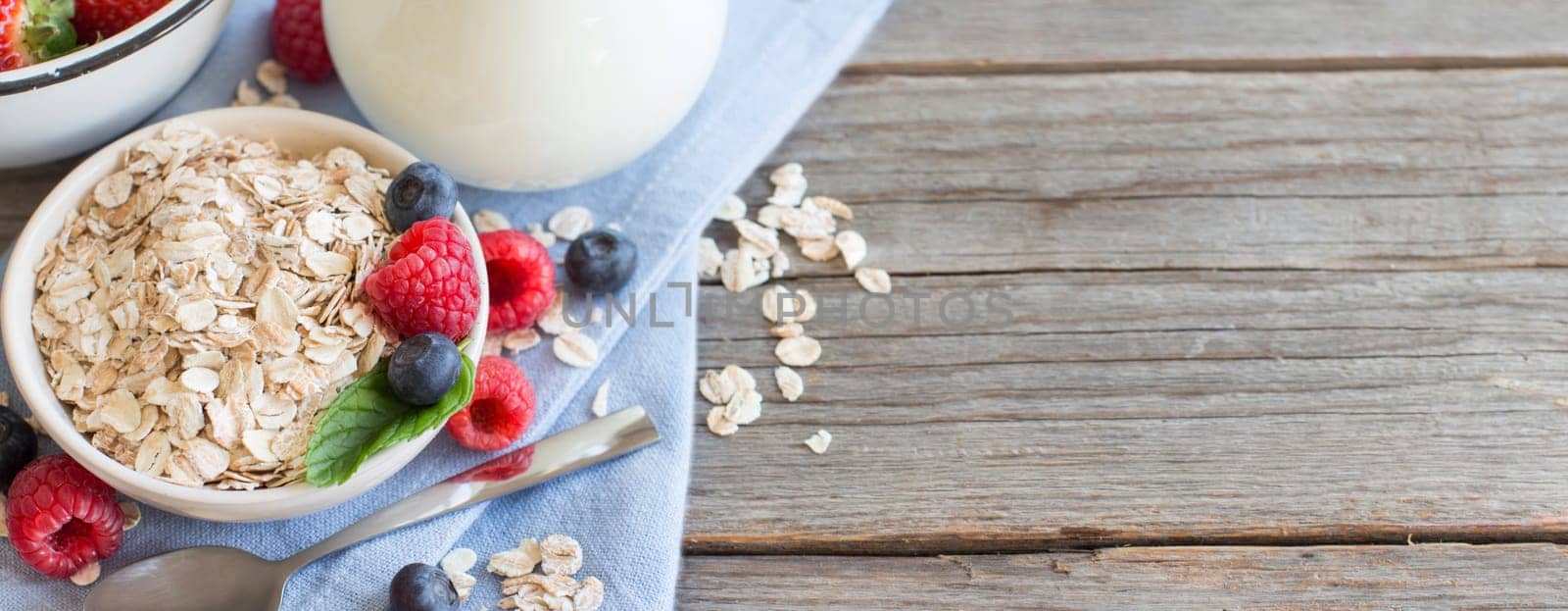 Rolled oats in a bowl with berries and milk on wood