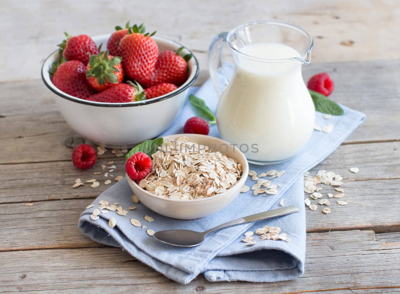 Rolled oats in a bowl with berries and milk on wood