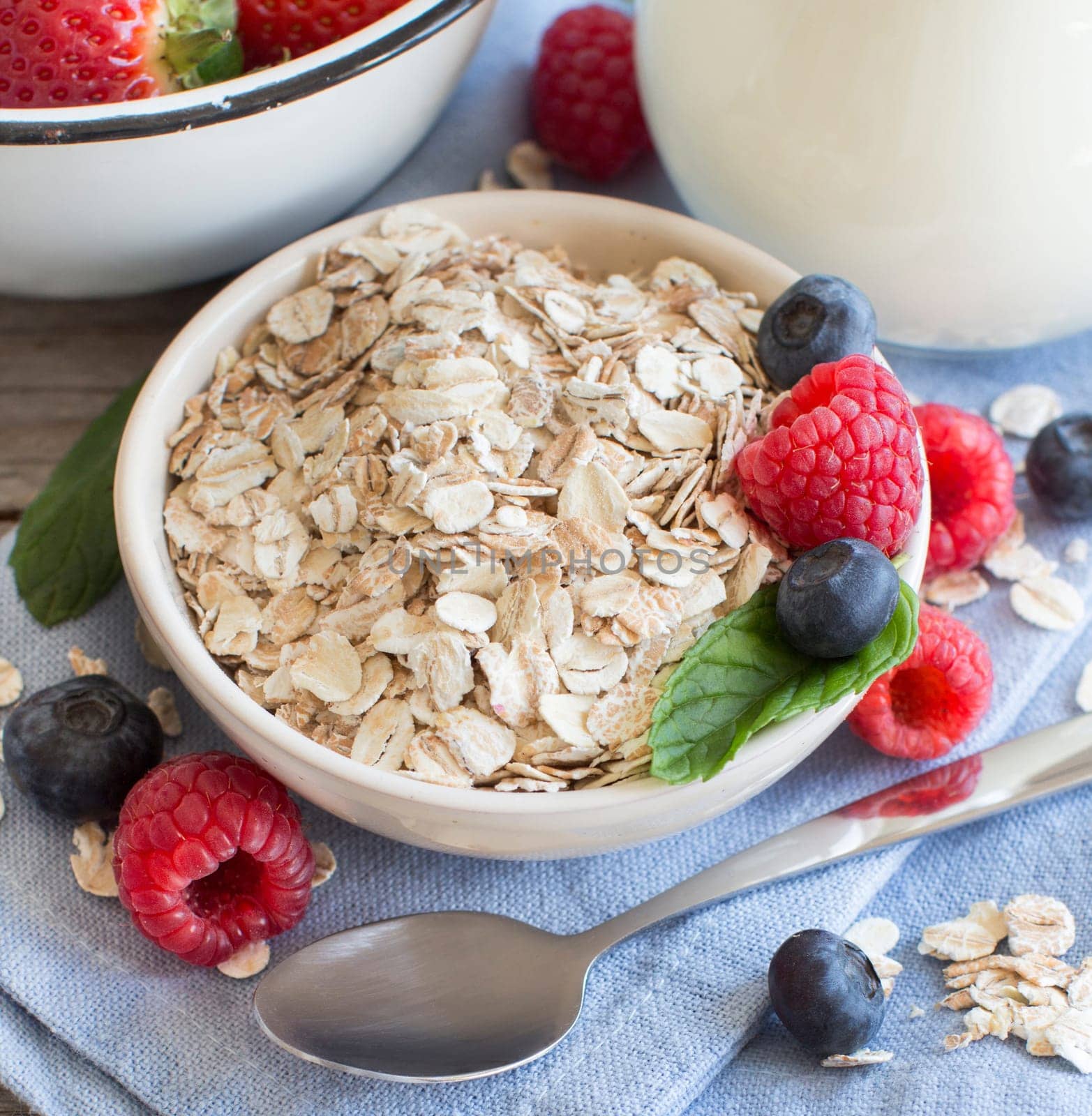 Rolled oats in a bowl with berries and milk on wood