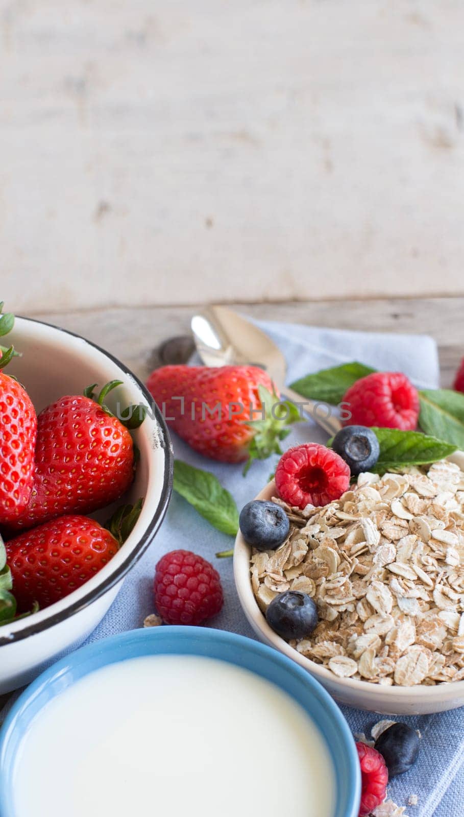 Rolled oats in a bowl with berries and milk on wood