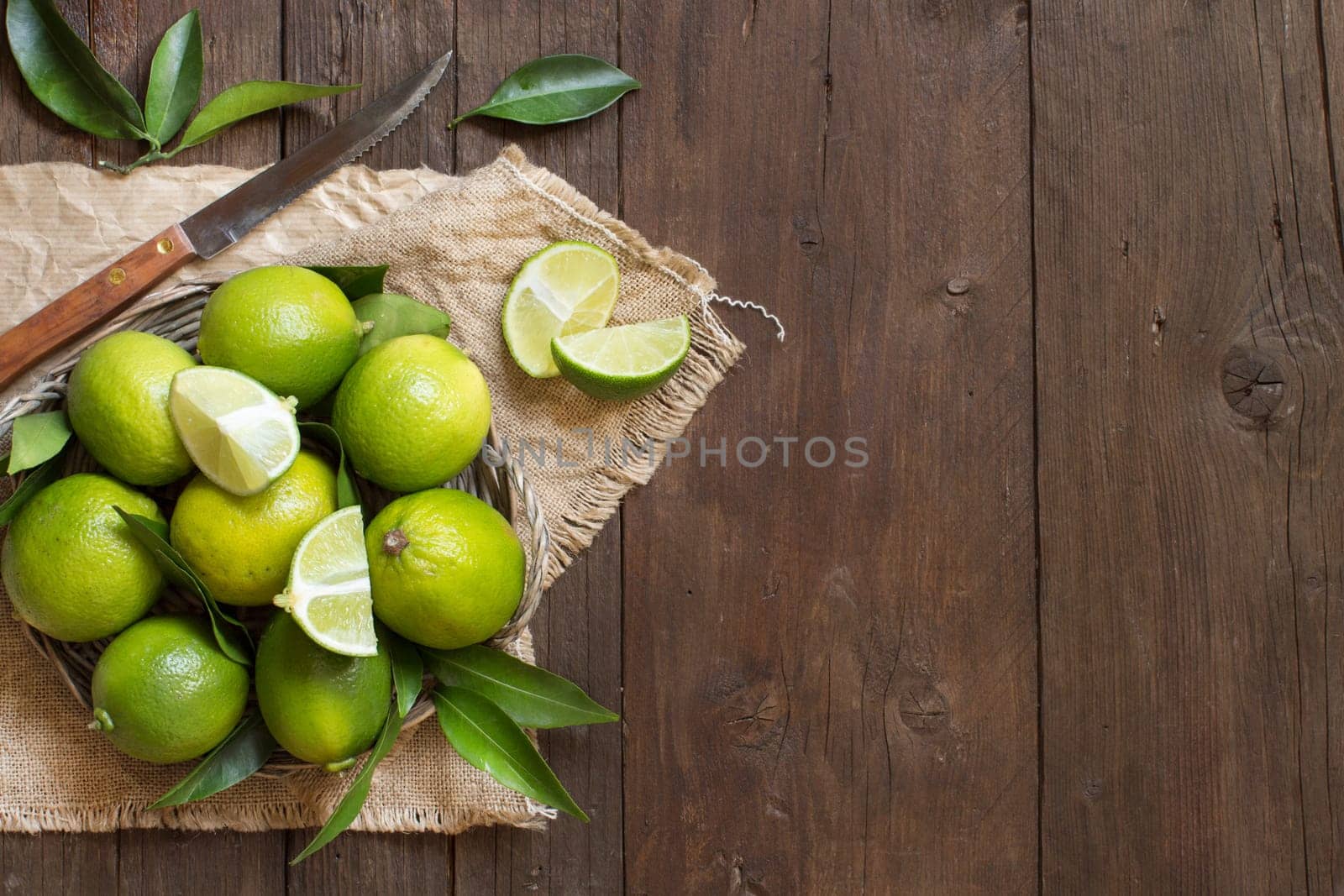 Fresh limes with knife and leaves on a wooden table