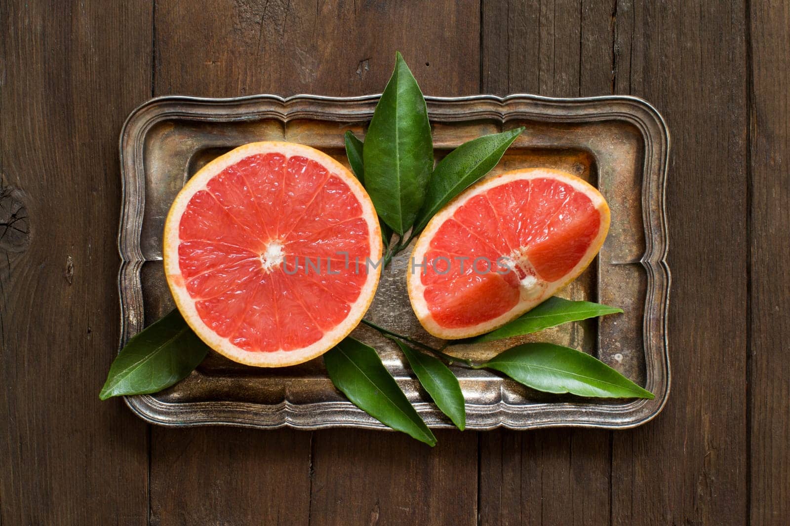 Fresh grapefruit with leaves on a tray on a wooden table