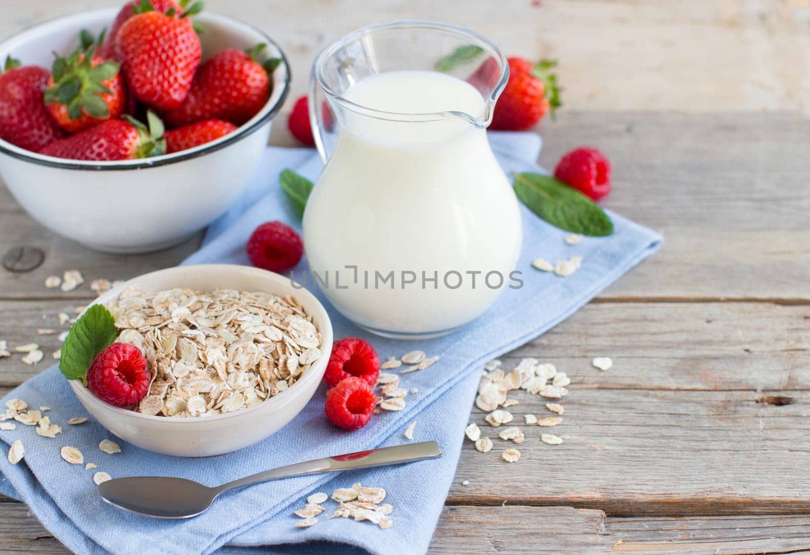 Rolled oats in a bowl with berries and milk on wood