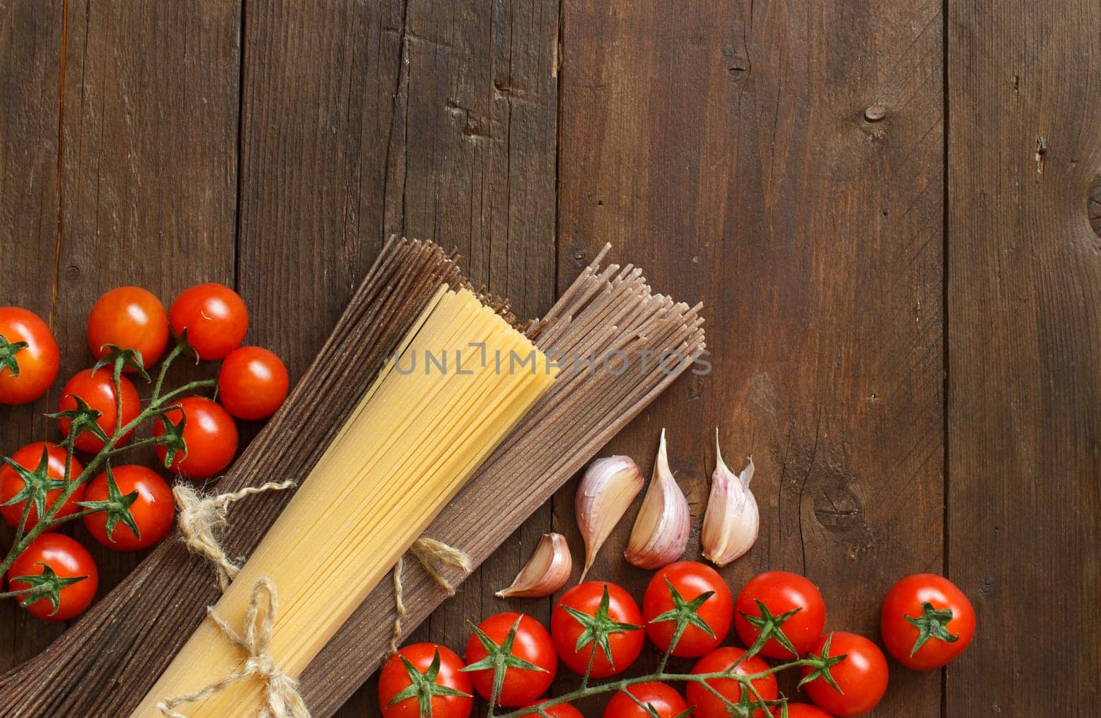 Three types of spaghetti, tomatoes and garlic on wood