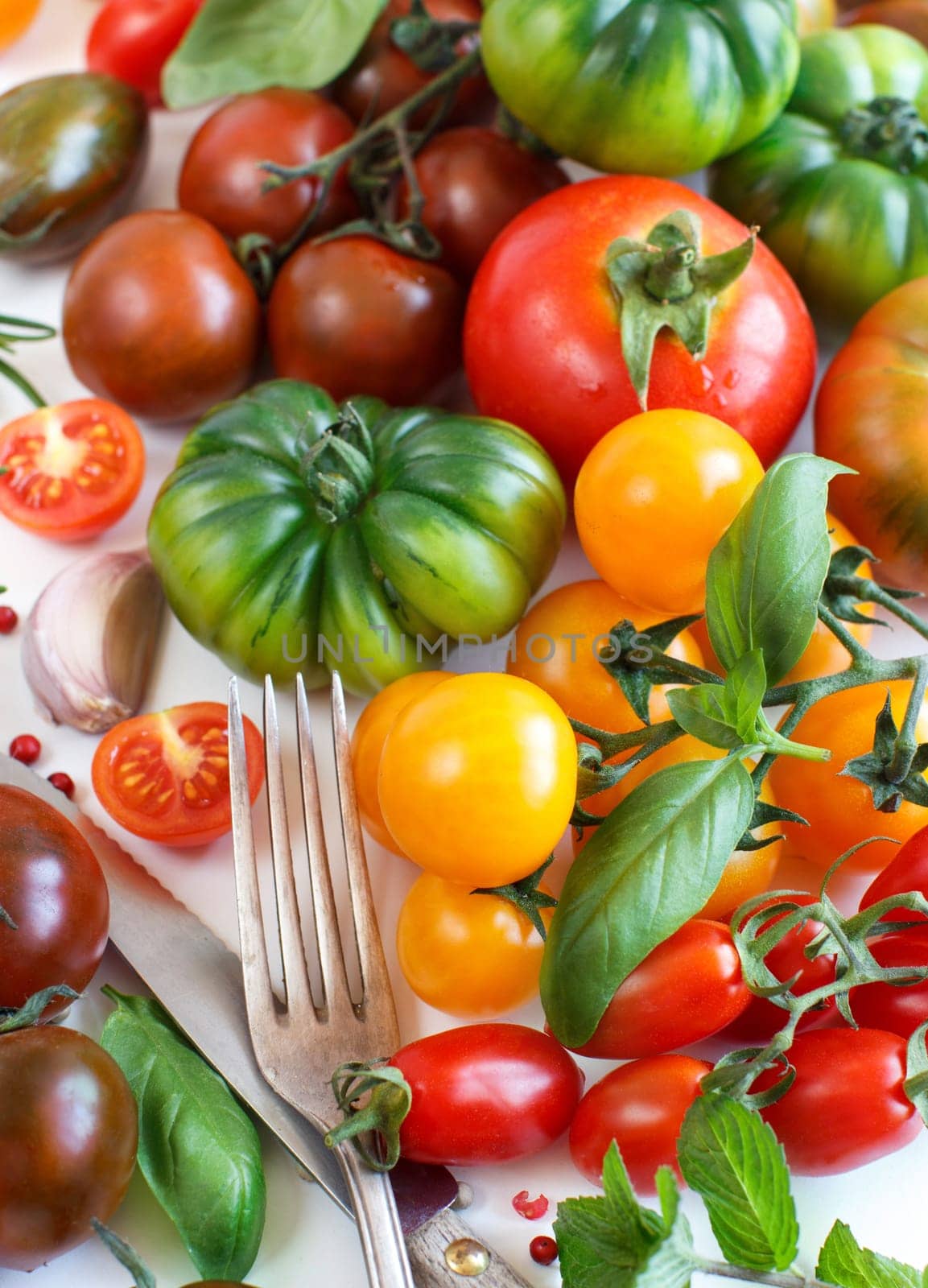 Colorful tomatoes, garlic, basil, fork and knife