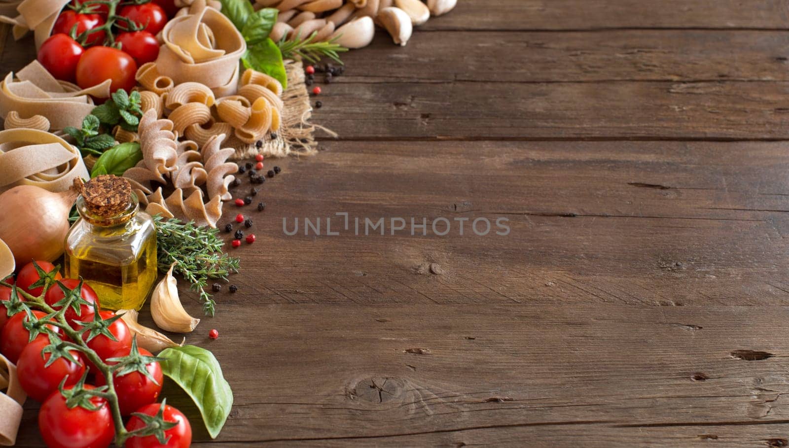 Whole wheat pasta, vegetables, herbs and olive oil on wooden background