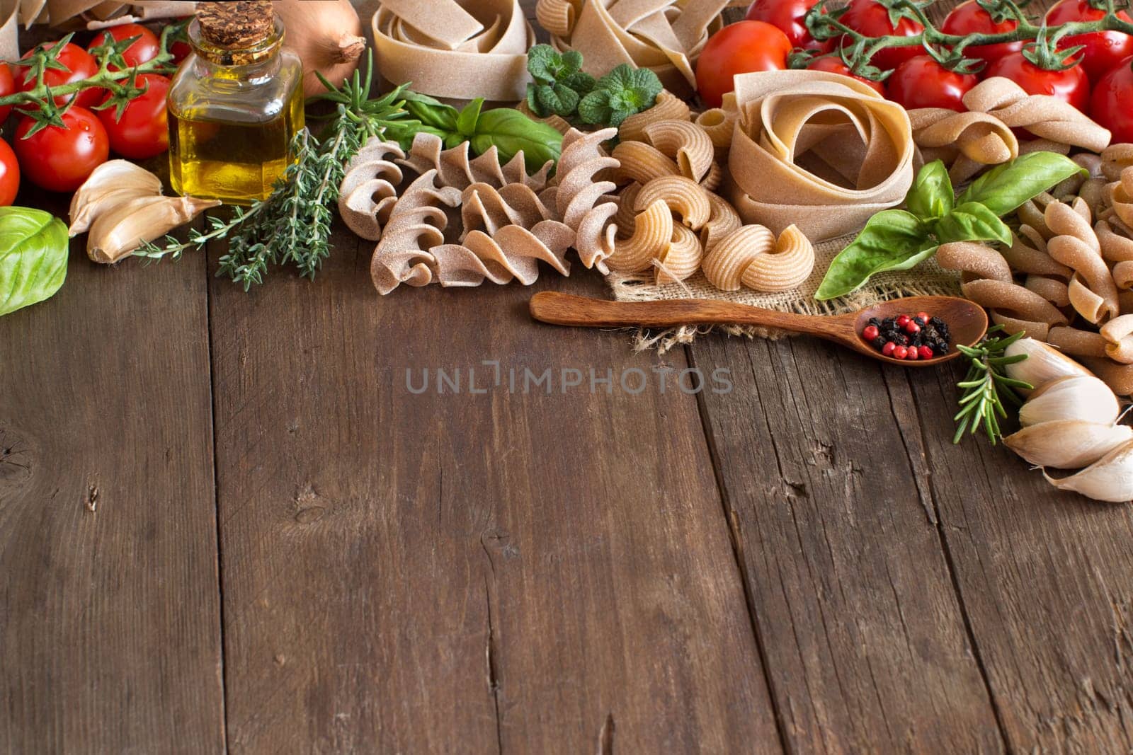 Whole wheat pasta, vegetables, herbs and olive oil on wooden background