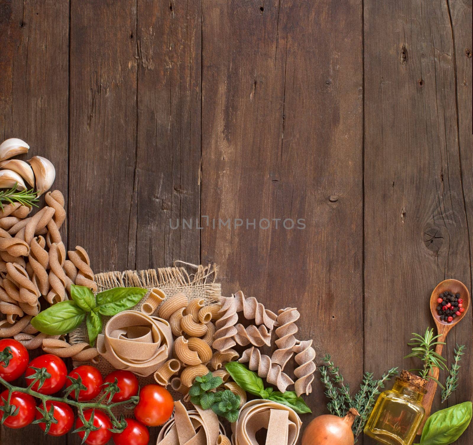 Whole wheat pasta, vegetables, herbs and olive oil on wooden background