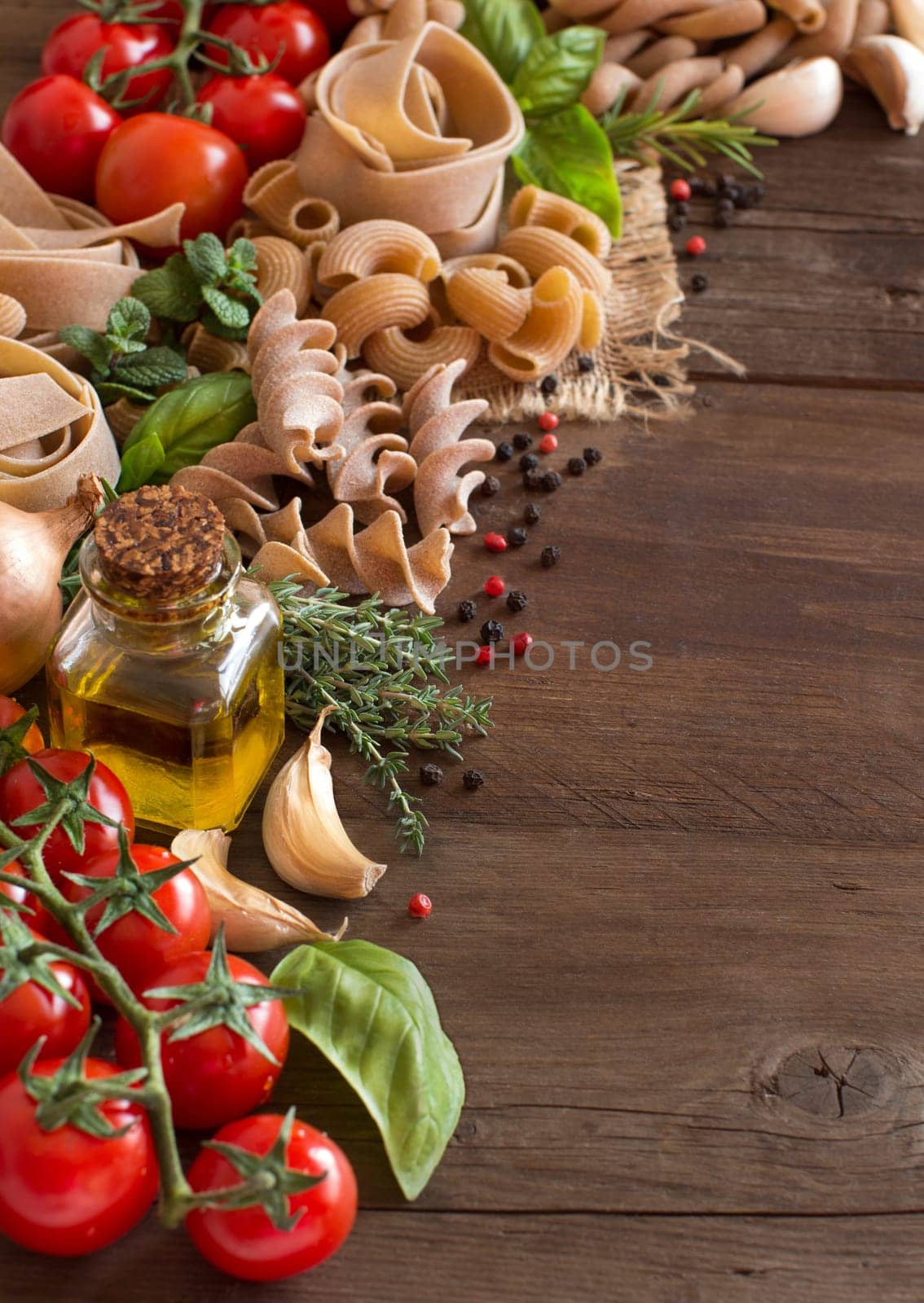 Whole wheat pasta, vegetables, herbs and olive oil on wood