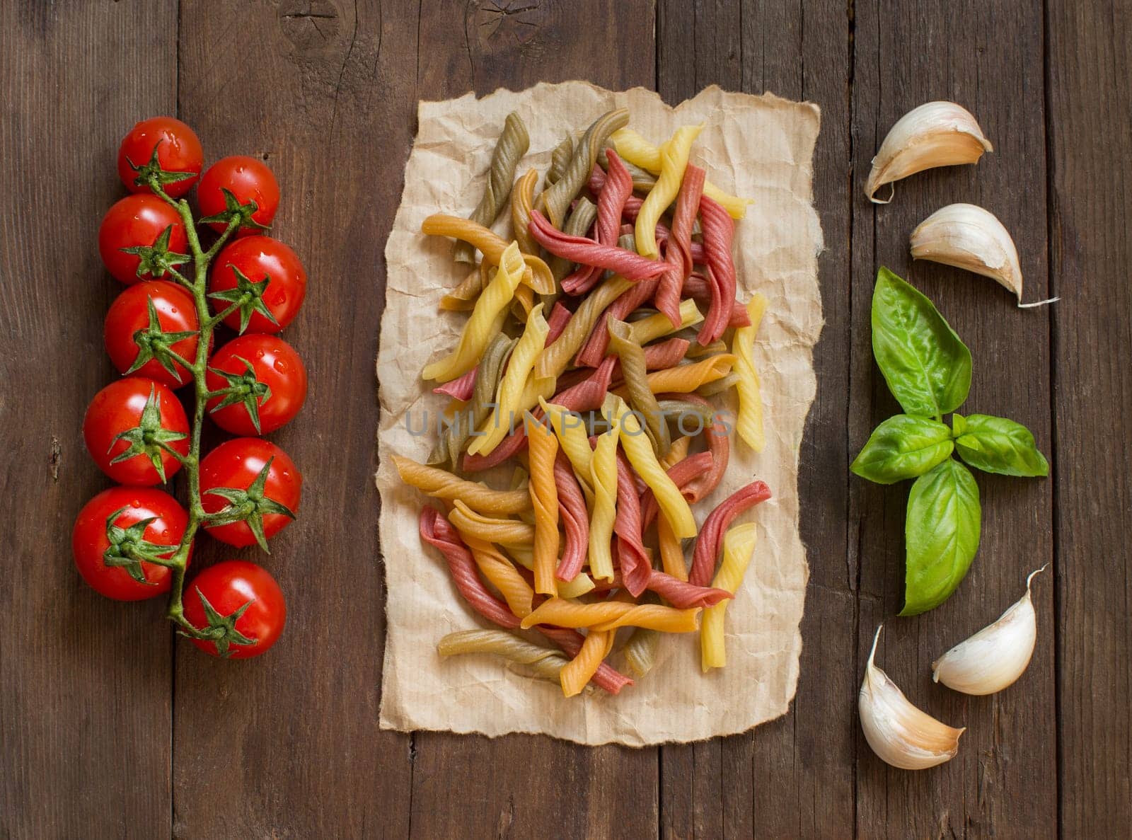 Tricolor pasta with cherry tomatoes, garlic and basil on wooden background