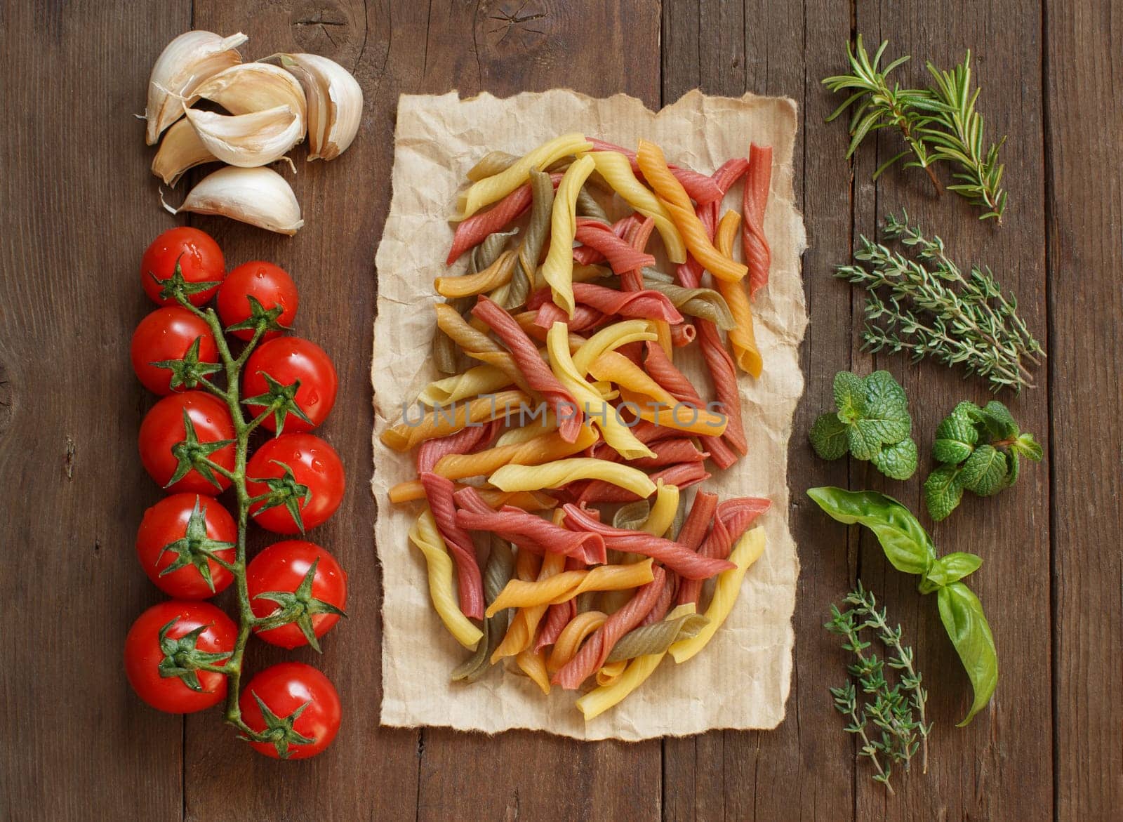 Colorful pasta, vegetables and herbs on wooden background